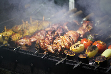 Pork, quail and vegetable barbecue on skewers frying on a grill brazier. Closeup