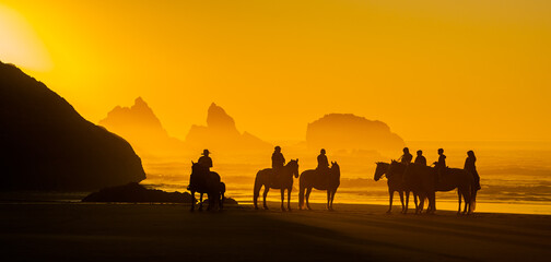 Fototapeta na wymiar Horseback riders on the beach at Bandon, on the southern Oregon coast, at sunset