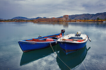 Fototapeta na wymiar Fishing motorboats on a lake with a castle ruins on a rainy day