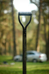 Black ragged shovel handle on the blurred background of a car in the woods