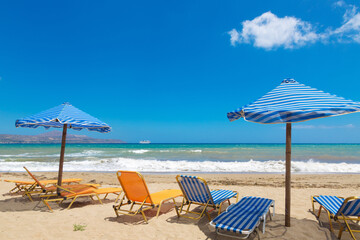Crete beach Kalyves. Blue and yellow umbrellas and sunbeds against the backdrop of a beautiful blue sea on a sunny day. Public beach Kalyves in Crete Island in Greece