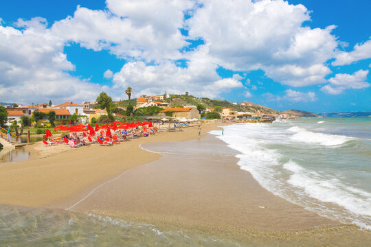 Kalyves,CRETE-GREECE:JULY 5 2017.The beach Kalyves.Red sunbed and umbrellas, people on background houses of villgage.
