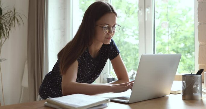 Attractive young student woman wears eyeglasses typing on computer searching information, enjoy web surfing, having study learning or working process using internet modern technologies, apps concept