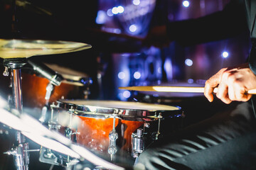 View of drum set kit on a stage during jazz rock show performance, with band performing in the background, drummer point of view