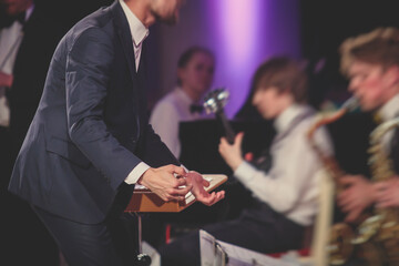 Young male Conductor directing symphony orchestra with performers in the background, the philharmonic venue hall during jazz concert