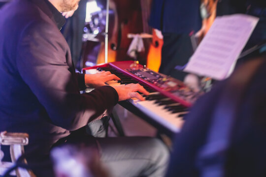 Concert view of a musical keyboard piano player during musical jazz band orchestra performing, keyboardist hands during concert, male pianist on stage