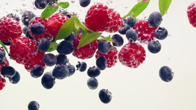 Raspberries, blueberries, mint splashing in the water on a white background