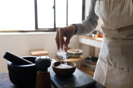 Mid section of woman in apron sprinkling rock salt in wooden bowl