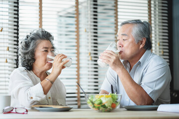 Smiling Asian senior man and woman drinking glasses of milk at home