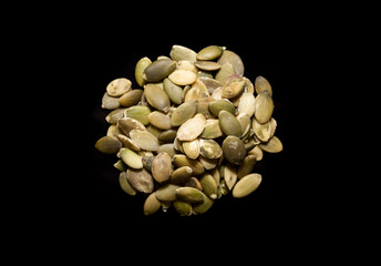 Looking down on a pile of pumpkin seeds on a black surface.