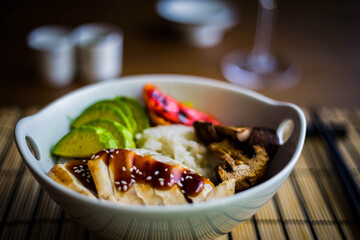 Asian rice bowl with grilled chicken breast, avocado, portobello mushrooms and peppers. Chopsticks on the background.