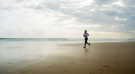 Naklejka premium wide lens silhouette of afro American runner woman jogging on the beach - young attractive and athletic black girl training outdoors doing running workout at the sea
