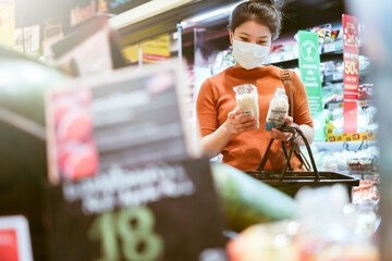 new normal after covid epidemic young smart asian female shopping new lifestyle in supermarket with face shild or mask protection hand choose fresh vegetable of fruit new normal lifestyle