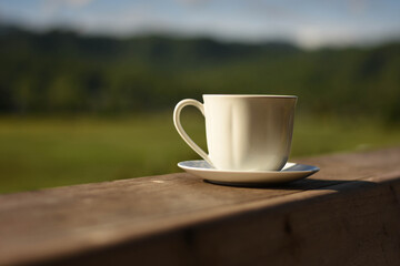 white cup of coffee on wooden table,blur background,sunlight.