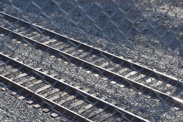 Two parallel railroad tracks, viewed diagonally through chain link fence.