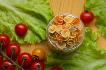 Pasta with vegetables in a plate. Ingredients for cooking tomatoes, cherry greens.  With basil. Background from spaghetti. On the table, top view. 
