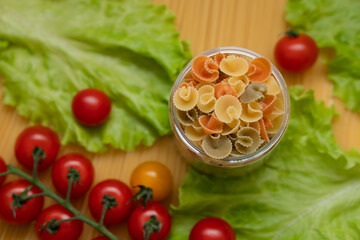 Pasta with vegetables in a plate. Ingredients for cooking tomatoes, cherry greens.  With basil. Background from spaghetti. On the table, top view. 