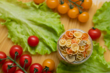 Pasta with vegetables in a plate. Ingredients for cooking tomatoes, cherry greens.  With basil. Background from spaghetti. On the table, top view. 