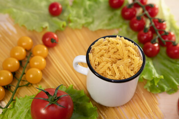 Pasta with vegetables in a plate. Ingredients for cooking tomatoes, cherry greens. Background from spaghetti. White enameled mug.