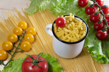 Pasta with vegetables in a plate. Ingredients for cooking tomatoes, cherry greens. Background from spaghetti. White enameled mug.
