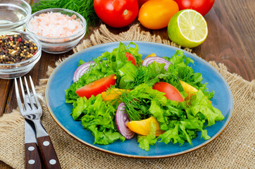 Light meal of green leaves of lettuce, yellow and red tomatoes, olive oil on wooden table.