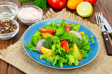 Light meal of green leaves of lettuce, yellow and red tomatoes, olive oil on wooden table.