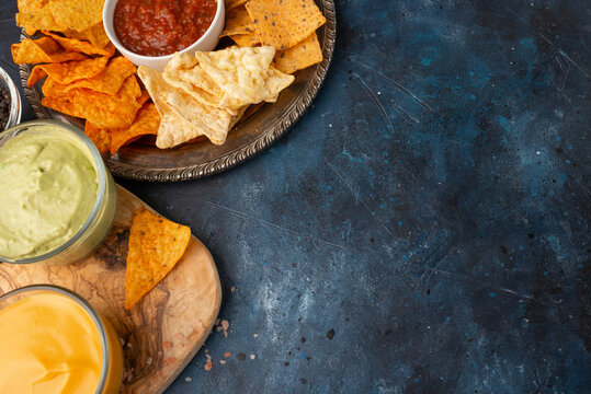 A Plate Of Various Snacks, Potato Chips, Pita Chips Served With Cheese, Avocado, Rosemary, And Salt Dip On A Blue Background. View From Above. Copy Space