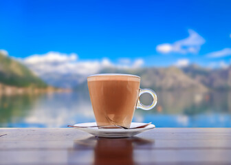 Cup of latte coffee with a blurred view of Kotor Bay or Boka Kotorska in background in Montenegro, on the Adriatic Sea