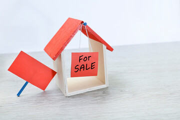 A toy house with for sale message hanging and a placard leaning over on the toy house 