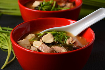 Japanese miso soup in two red Japanese bowls on the black table. Miso soup with tofu, tuna, herbs and seaweed with white Japanese soup spoon and red chopsticks.