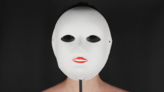 Brunette puts on a white theater mask. Theatrical makeup sad mask. Girl hides emotions behind a mask.