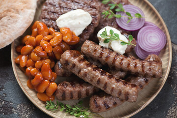 Closeup of serbian traditional grilled cevapi sausages and pljeskavicas with kajmak, prebranac and red onion, selective focus