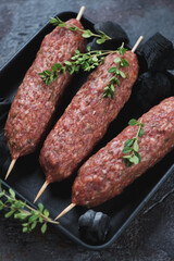 Close-up of raw fresh lula-kebabs made of beef meat with thyme, vertical shot, selective focus