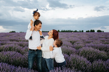 Young happy family: father, mother, son and daughter are in the middle of the lavender field and looking at each other