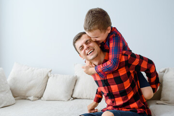 Laughing father and his son, in same plaid shirts are playing and having fun.