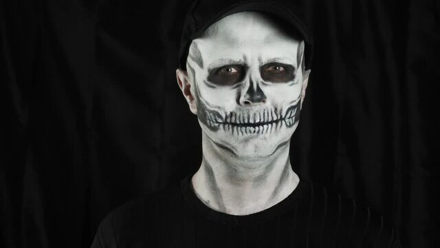 Makeup skeleton for Halloween. Human skeleton on a dark background. A man shows a heart shape in his hands.