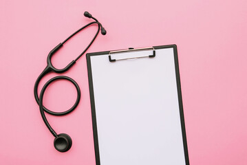 Black modern stethoscope and blank medical form on pink background.