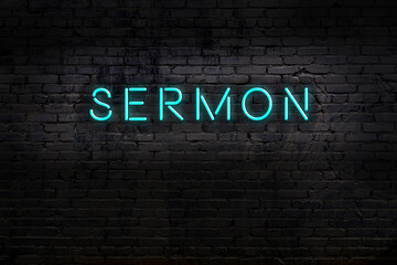 Night view of neon sign on brick wall with inscription sermon