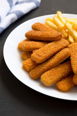 Homemade Fish Sticks and Fries on a white plate on a black background, side view. Close-up.