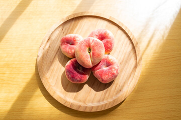 A plate of fresh flat peaches on a wooden table
