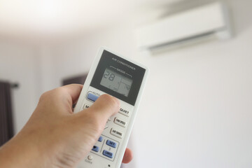 Hand with remote control directed on air conditioner inside the room
