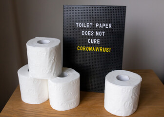 a word bord with the quote 'toilet paper does not cure corona virus' with toilet paper stacked up next to it