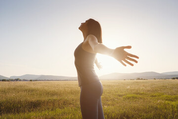 Young girl spreading hands with joy and inspiration facing the sun