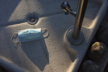 Mask on the floor of a community pool shower at sunset, concept sanitary standards with copy space.