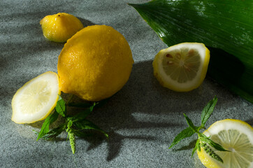 Whole lemon and pieces of one, mint leaves on the grey wet surface.Ingredients for cold citrus...