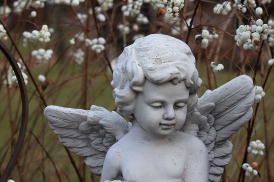 A decorative white angel figure on a graveyard in front of white flowers. Concepts of faith, death, innocence, childhood and after life.