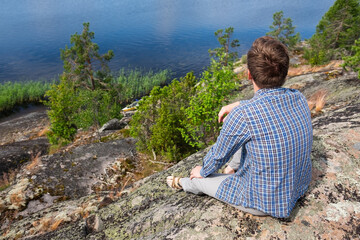 Naklejka premium Caucasian man stopping for rest on countryside walk sitting alone on stone near lake.