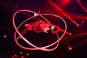 Flexible young woman make performance on aerial hoop, flexible back on aerial hoop, aerial circus show, blue and red light. Flexible woman gymnast upside down on hoop. Night club performance