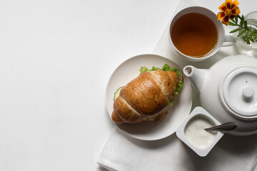 Breakfast in a white bowl on a light background classic croissant, herbal, green tea, flower, fruit, yogurt