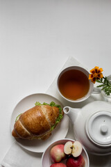 Breakfast in a white bowl on a light background classic croissant, herbal, green tea, flower, fruit, yogurt
